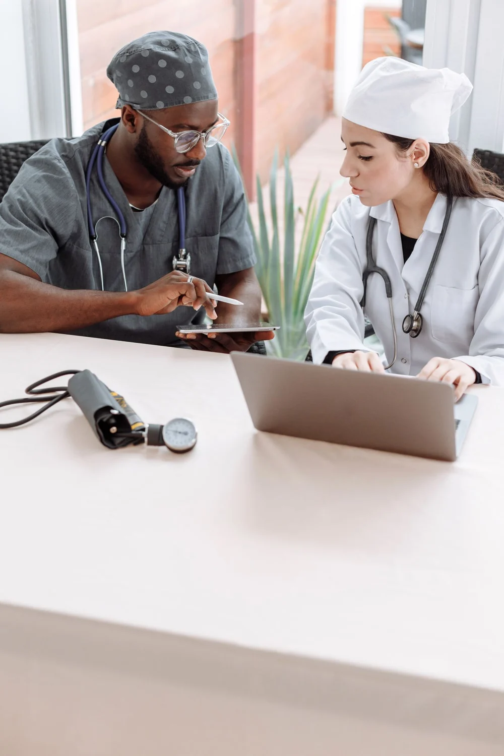 Two healthcare professionals discussing a tablet beside a laptop